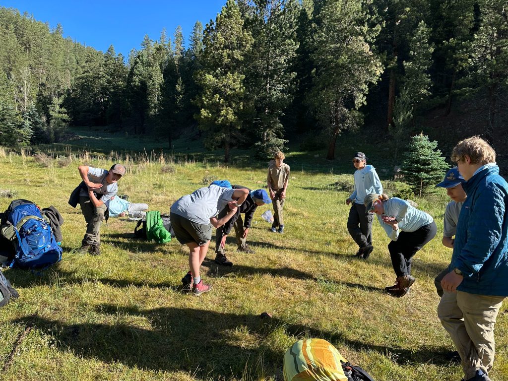 Group of people practicing outdoor skills in a grassy area surrounded by trees.